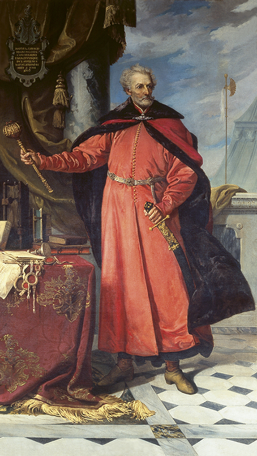 „Jan Zamoyski, I ordynat”, Józef Buchbinder, 1890; Polska, Warszawa „Jan Zamoyski, I ordynat”, Józef Buchbinder, 1890; Polska, Warszawa; wymiary 299x172 cm; Materiał/technika: płótno, olej
Całopostaciowe przedstawienie starszego mężczyzny. Twarz wychudła, nos ostry, lekko zakrzywiony, czoło wysokie. Włosy krótkie, zmierzwione, siwe, tak jak wąsy i krótka, gęsta broda. Ubrany w czerwony żupan, przepasany ozdobnym pasem. Na ramionach czerwony płaszcz obszyty futrzanym brązowym kołnierzem i podbiciem, pod szyją spięty ozdobną broszą. Mężczyzna lewą rękę opiera na rękojeści szabli przymocowanej do pasa a w prawej, wyciągniętej w bok, złotą, nasadzaną kamieniami buławę. Po prawej stronie postaci stół nakryty purpurową narzutą ze złotymi frędzlami i złotym haftem. Na stole księgi, rozłożone dokumenty, tłok pieczętny i pieczęcie. Nad stołem drapowana, ciężka oliwkowa kotara odsłaniająca fragment kolumny. Na tle kotary kartusz z herbem Jelita i napisem: „Joannes de Zamoscio Regni Poloniae Cancellarius”. Za kanclerzem fragment kamiennej balustrady, w głębi zarys spadzistego dachu na tle lekko zachmurzonego nieba.