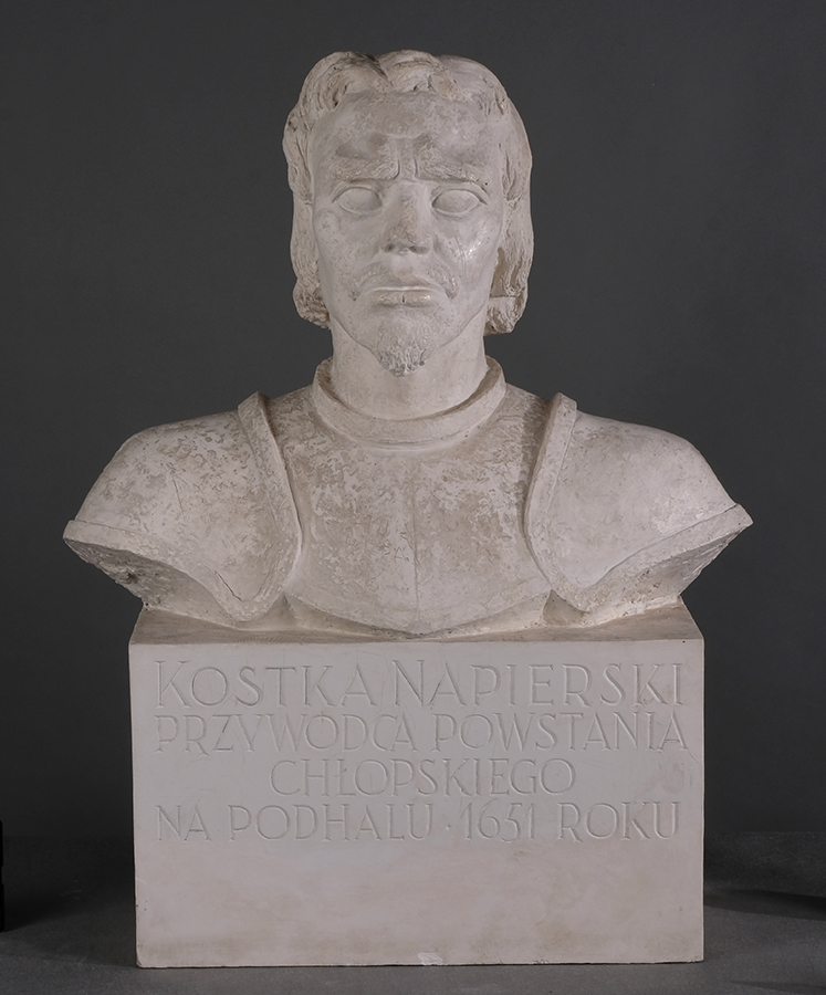 Karol Tchorek, Popiersie Kostki-Napierskiego, 1951, gips, odlew, 93 x 58 x 32 cm; nr inw. MPK/SW/1078 Fotografia przedstawia gipsową rzeźbę autorstwa Karola Tchorka, zatytułowaną Kostka Napierski, wykonaną w 1951 roku. Popiersie młodego mężczyzny w pancerzu z naramiennikami. Głowa prosto osadzona na dość długiej szyi, twarz trójkątna z dość wysokim czołem, wystającymi kośćmi policzkowymi i krótkim szerokim nosem. Duże oczy pod zmarszczonymi brwiami, usta o pełnych wargach, wąsy i hiszpańska bródka. Włosy lekko kędzierzawe, zakrywające uszy. Na wysokim prostopadłościennym postumencie napis KOSTKA NAPIERSKI PRZYWÓDCA POWSTANIA CHŁOPSKIEGO NA PODHALU 1651 ROKU.
