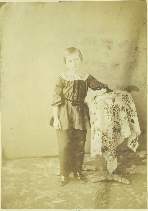 Konstanty Zamoyski (1846 - 1923), początek lat 50. XIX wieku; zbiory Muzeum Zamoyskich w Kozłówce, nr inw. MPK/F/156 Fotografia archiwalna przedstawia kilkuletniego chłopca w całej postaci stojącego przy stoliku. Chłopiec ubrany w ciemny strój (surducik i spodnie), na szyi biały szeroki kołnierzyk. Włosy gładko ułożone. Stolik nakryty białym obrusem dekorowanym ciemnymi kwiatami. Tło neutralne. Fotografia w kolorze sepii.
