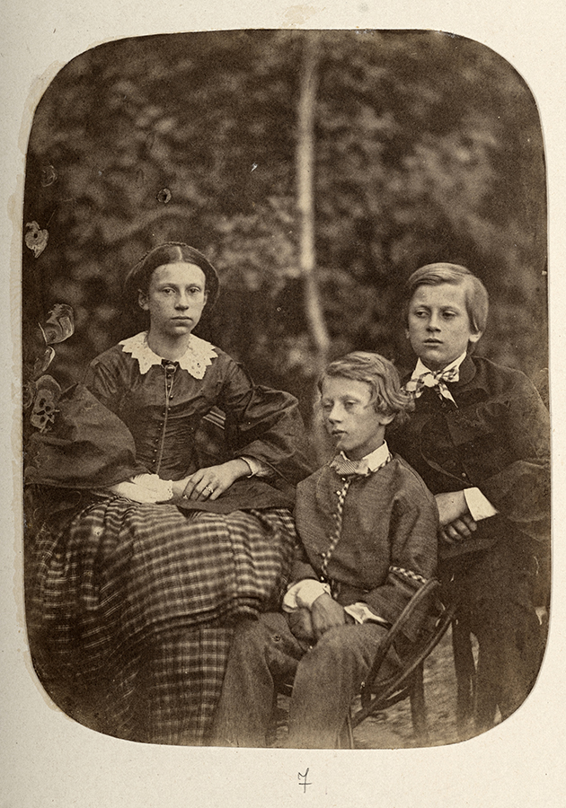 Jadwiga (1844 - 1895), Konstanty (1846 - 1923) i Jan (1849 - 1923) Zamoyscy, dzieci Jana Zamoyskiego i Anny z Mycielskich Zamoyskiej, Francja, około 1857 roku; zbiory Muzeum Zamoyskich w Kozłówce, nr inw. MPK/F/66 Fotografia archiwalna przedstawia troje dzieci w różnym wieku: od lewej strony kilkunastoletnia dziewczynka i dwóch młodszych chłopców. Siedzą na fotelach, w ogrodzie, na tle drzew. Dziewczynka w ciemnej bluzce z bufiastymi rękawami i białym kołnierzykiem, w ciemnej spódnicy w kratę. Włosy ułożone gładko, z przedziałkiem pośrodku i spięte z tyłu. Starszy chłopiec, siedzący z tyłu, ubrany w ciemny garnitur i białą koszulę, włosy ułożone gładko z przedziałkiem po prawej stronie. Młodszy chłopiec, w nieco jaśniejszym garniturze i białej koszuli, włosy nieco dłuższe, z przedziałkiem po lewej stronie, lekko pofalowane. Fotografia w kolorze sepii.